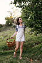 Woman in a field holding a basket, standing under a tree.