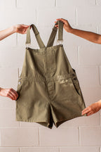 Green overalls held up against a light brick wall