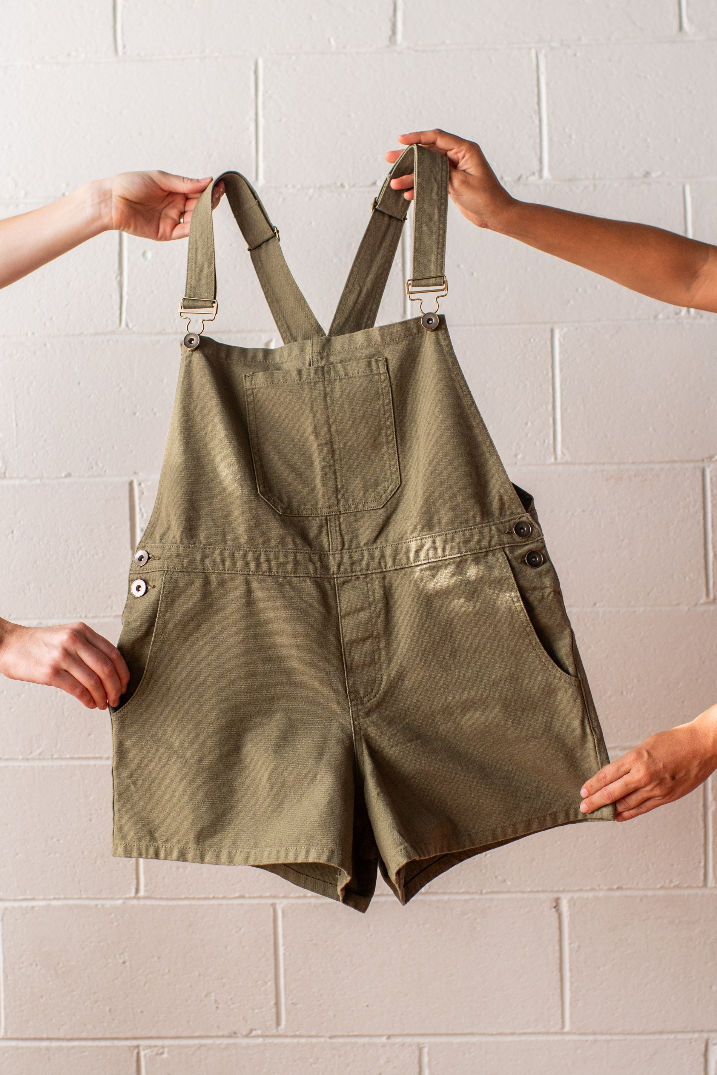 Green overalls held up against a light brick wall